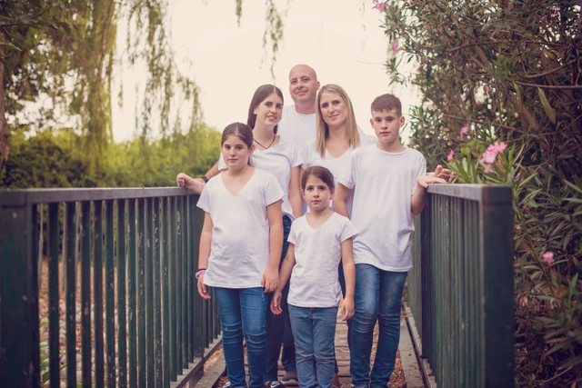 A family of six, including a mother, father, and four children, standing on a bridge outdoors.