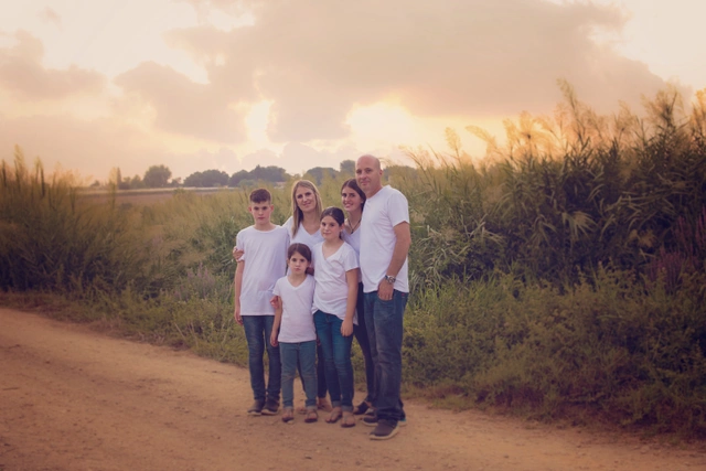 A family of six standing on a dirt path at sunset, surrounded by tall grass.