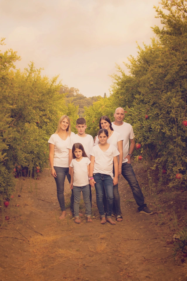 A family of five, parents and three children, standing in a pomegranate orchard.